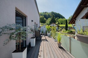 A wooden deck with potted plants, a table with chairs, and a view of a green landscape in the background. - OsWALD Holiday Apartment (Ettenheim)