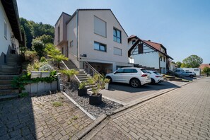 A residential building with a staircase leading to a garage, a parked white car, and a small garden area with potted plants. - OsWALD Holiday Apartment (Ettenheim)