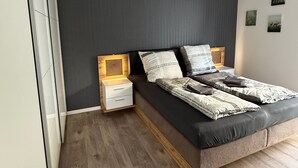 A modern bedroom with a bed, bedside tables, a wardrobe, and a wall-mounted light fixture. - OsWALD Holiday Apartment (Ettenheim)