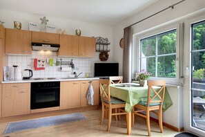 A kitchen with wooden cabinets, a stove, a sink, and a dining area with a table and chairs. - Apartment 'Talblick, 50 sqm' with Balcony and Wi-Fi (Glottertal)