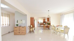 A spacious living room with a dining area, a kitchen in the background, and a wooden cabinet with drawers. - Seraina House (94QJ+W7M Pastida, Greece)