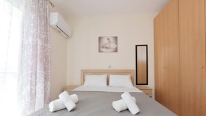 A neatly made bed with two rolled towels, a wooden wardrobe, a framed picture on the wall, and an air conditioning unit. - Seraina House (94QJ+W7M Pastida, Greece)