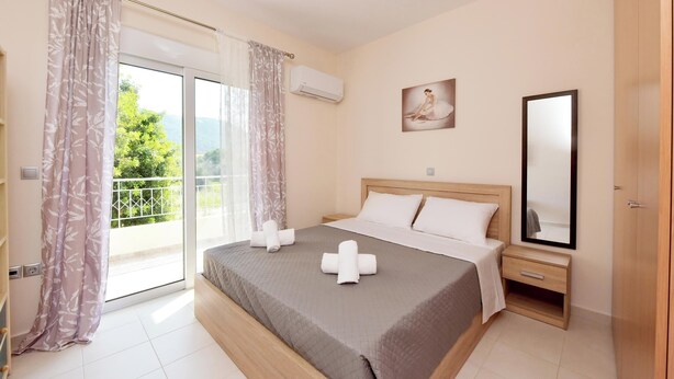 A bedroom with a bed, a nightstand, a mirror, and a window with curtains. - Seraina House (94QJ+W7M Pastida, Greece)