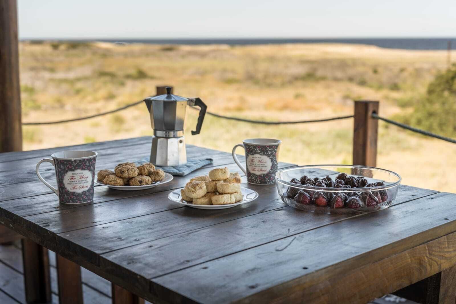 Une table en bois avec une cafetière, deux tasses à motifs floraux, une assiette de biscuits et un bol de fruits rouges.