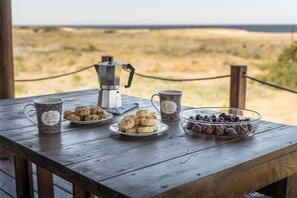 Une table en bois avec une cafetière, deux tasses à motifs floraux, une assiette de biscuits et un bol de fruits rouges.