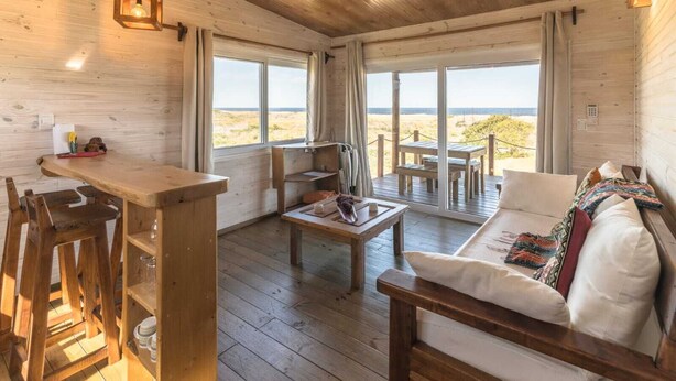 Un intérieur en bois avec un espace bar, des sièges et de grandes fenêtres donnant sur la plage.