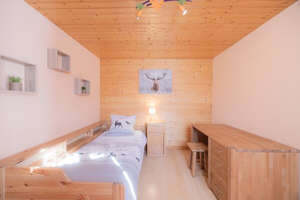 A cozy bedroom with a wooden ceiling, a bed with a deer-themed bedspread, a nightstand, a dresser, and a wall-mounted picture of a deer head.