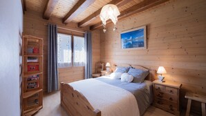 Ein Zimmer aus Holz mit einem Bett, Nachttischen, einem Bücherregal, einem Fenster mit Vorhängen und einem Bild an der Wand.