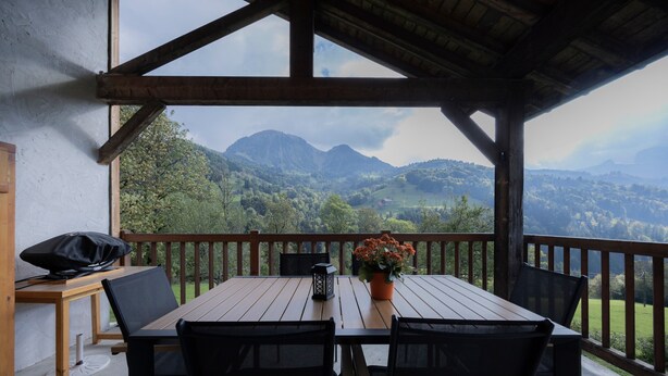 Eine Holzdielen-Terrasse mit Tisch und Stühlen, mit Blick auf eine gebirgige Landschaft.