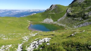 Eine gebirgige Landschaft mit einem kleinen See, felsigem Gelände und weit entfernten Berggipfeln.