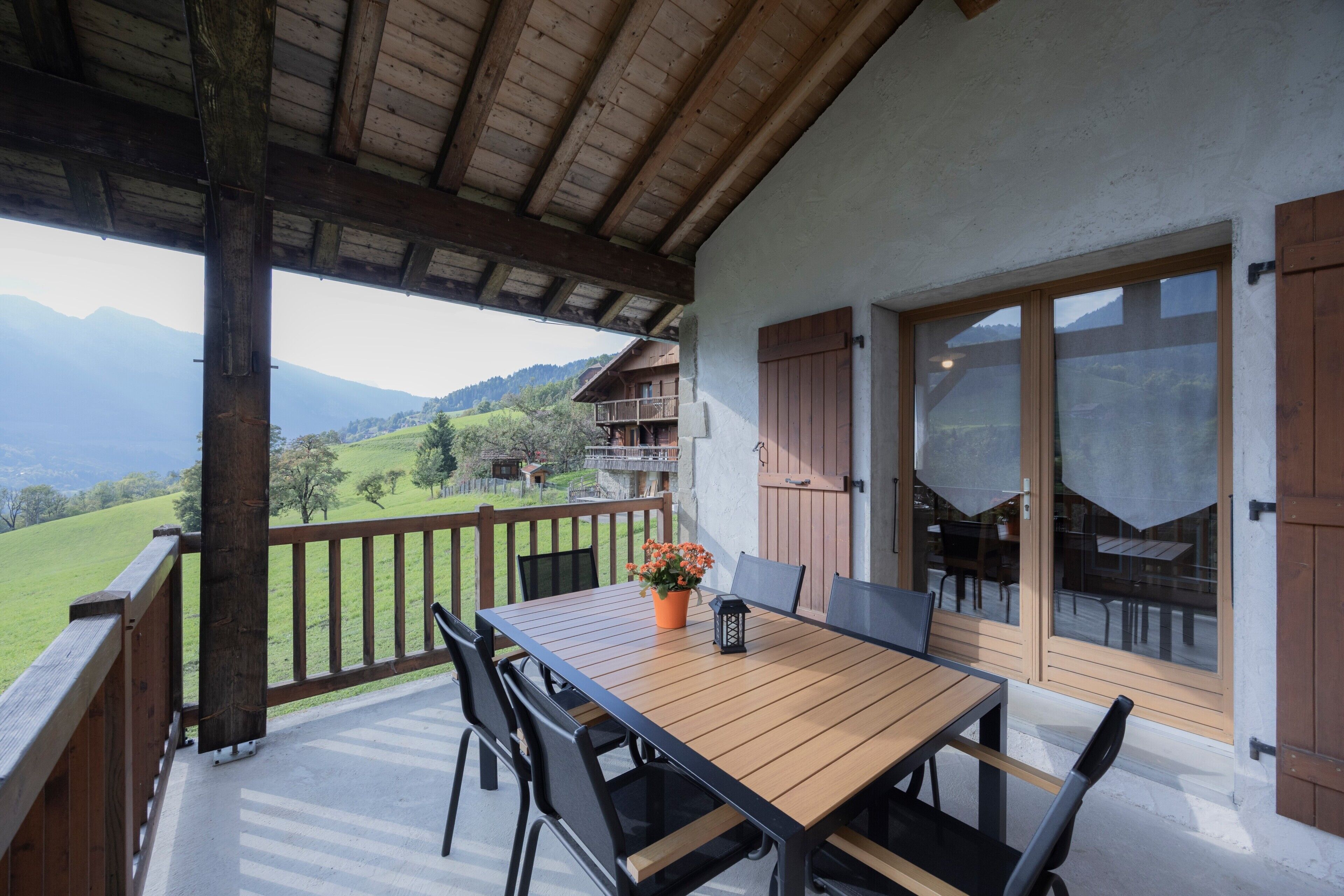 Une terrasse en bois avec une table et des chaises, un pot de fleurs et une vue sur un paysage montagneux.