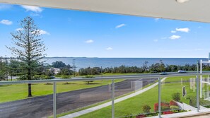A balcony with a view of a road, greenery, and the sea.