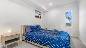 A bedroom with a bed, a nightstand, a small wooden cabinet, a window with a view, and a painting on the wall.