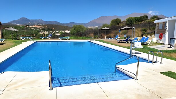 A rectangular swimming pool with a clear blue water, surrounded by a white deck, and a view of mountains in the background. - Apartment 'Best Sea Views' with Sea View, Wi-Fi and Air Conditioning (Málaga)