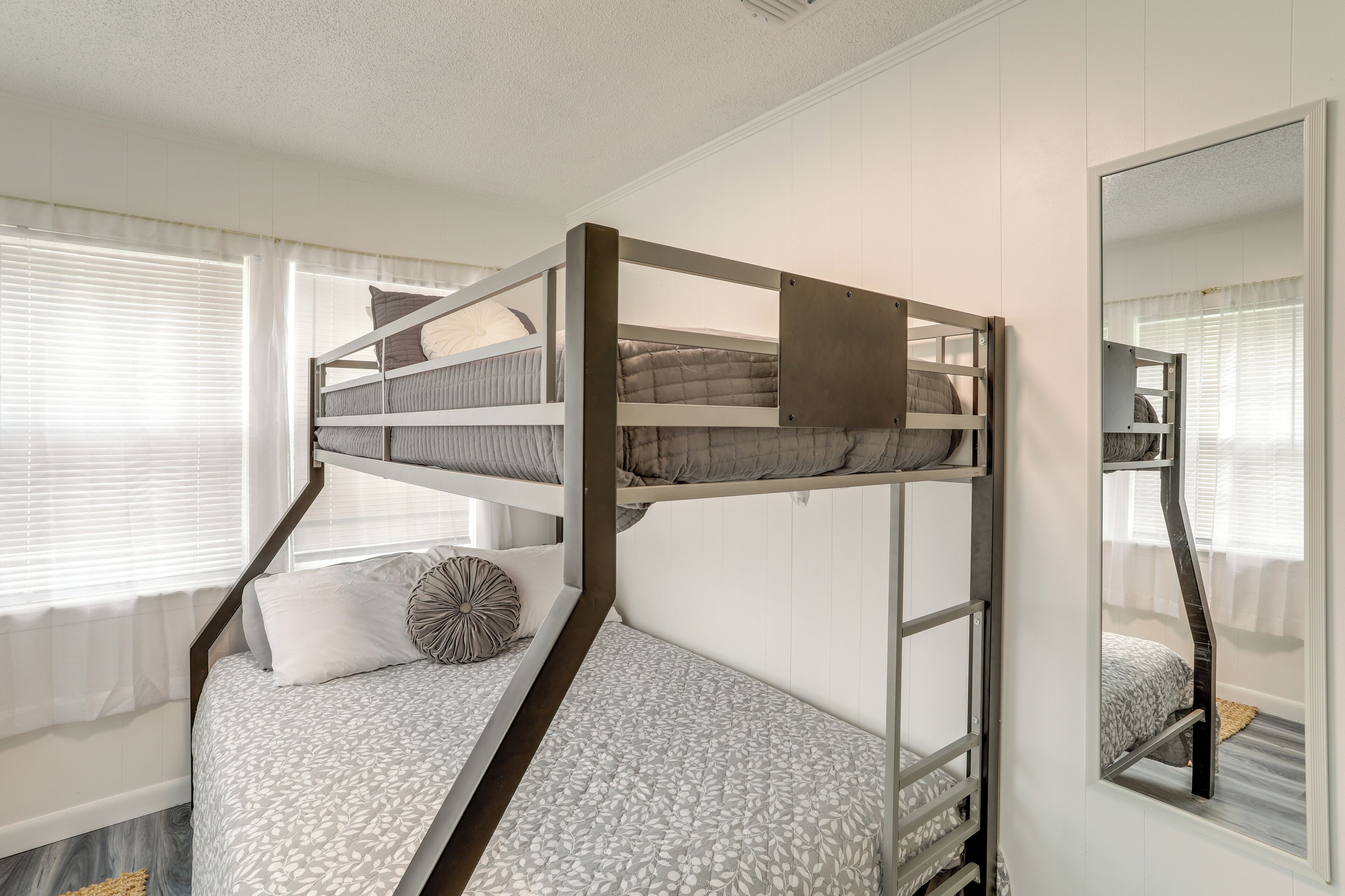 A bunk bed with a headboard, a window with blinds, and a mirror on the wall.