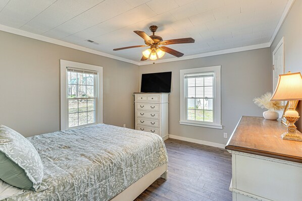 A bedroom with a bed, a dresser, a ceiling fan, and a TV on the wall. - Close to Shops, Eats & Hospital: Roxboro Retreat (Roxboro)