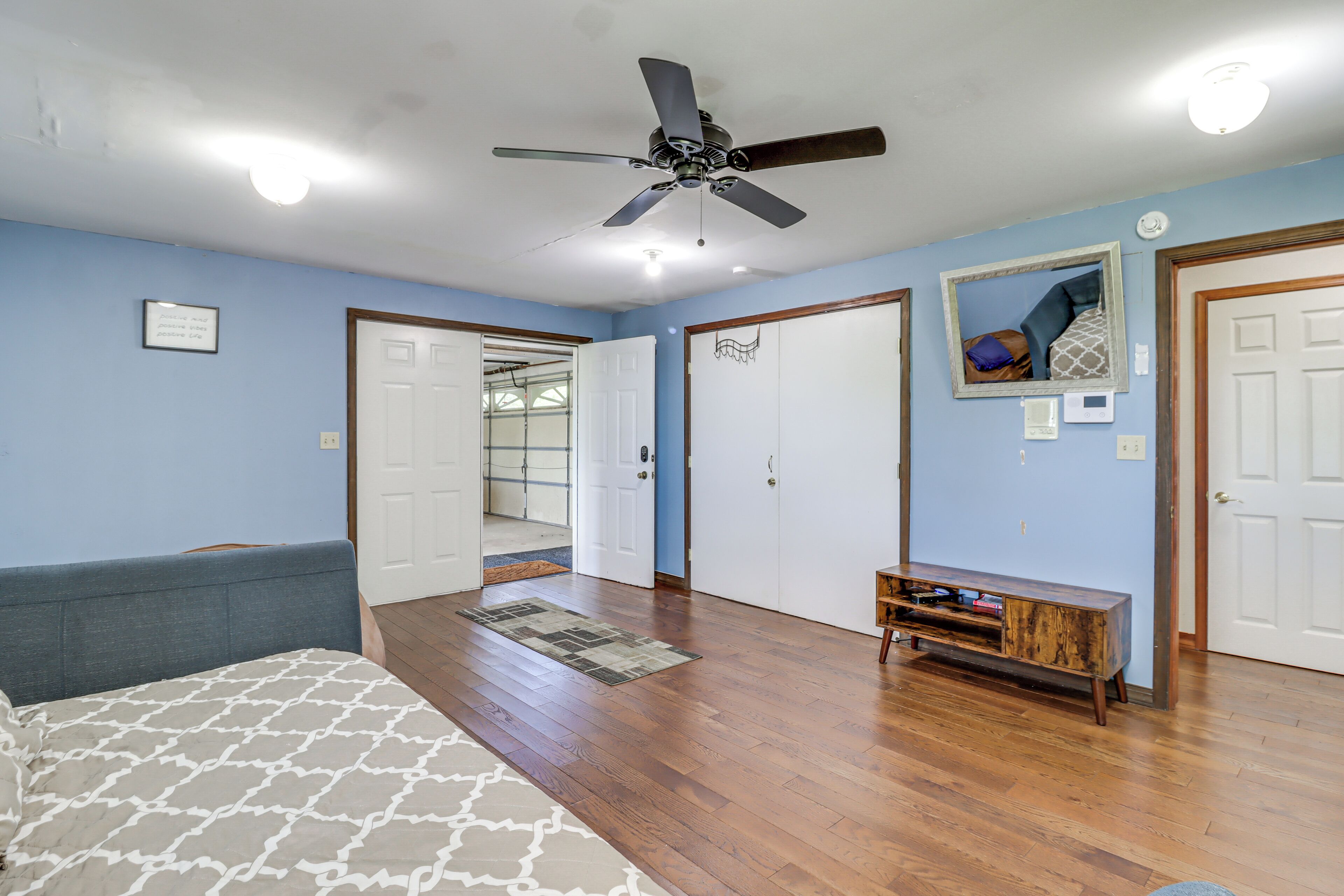 A bedroom with a bed, a ceiling fan, a wooden bench, and a door leading to another room.