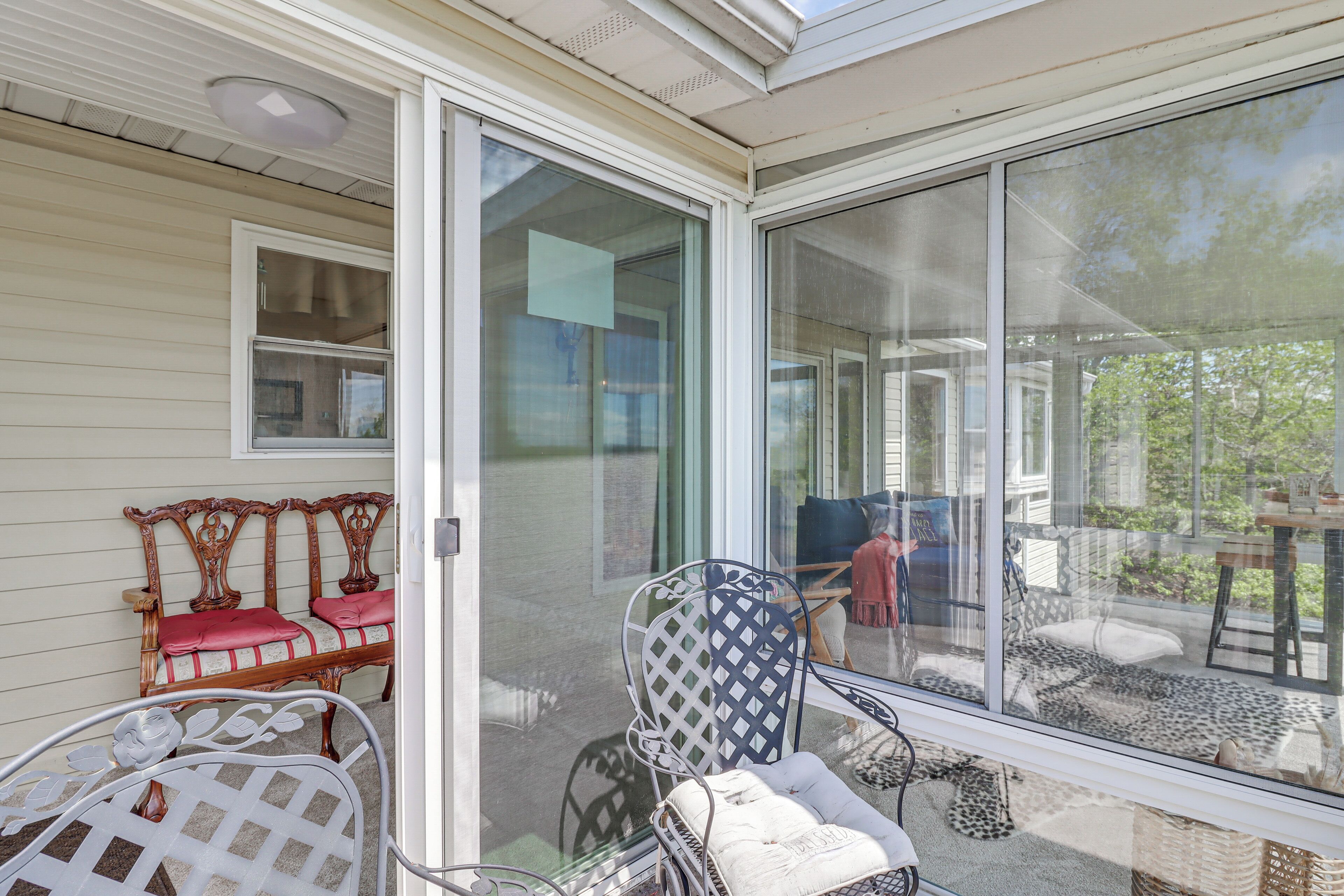 A sunroom with a sliding glass door, a wooden bench with cushions, and a metal chair.