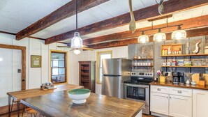 Una cocina con vigas de madera, una isla grande, electrodomésticos de acero inoxidable y lámparas colgantes.