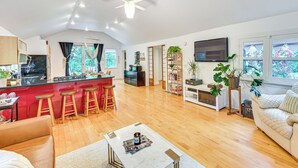 A spacious living area with a kitchen, wooden flooring, a ceiling fan, a TV, and a large window with a view of greenery. - Walk to Kelsey Lake: Cassopolis Home w/ Yard! (Cassopolis)