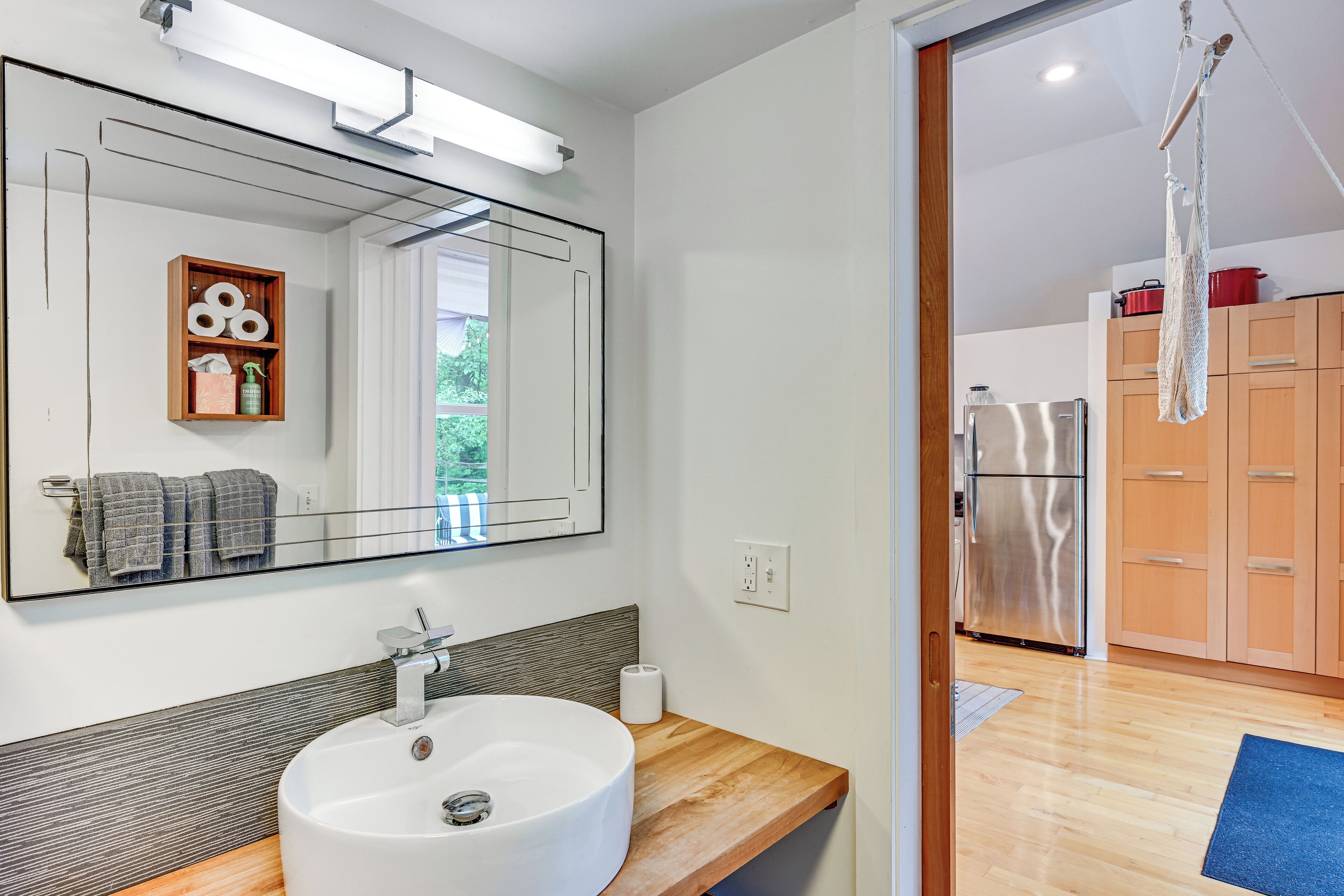 A modern bathroom with a large mirror, a round sink, and wooden cabinetry.