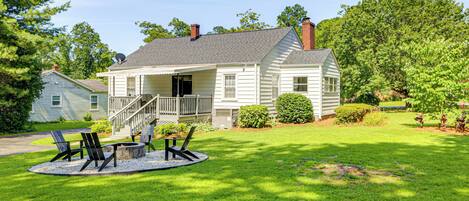 A white two-story house with a front porch, a fire pit, and outdoor seating.