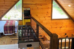 A cozy room with a foosball table, a bed with a plaid blanket, and a window overlooking greenery. - Riverside Retreat - Tranquility and Fun (McCaysville)
