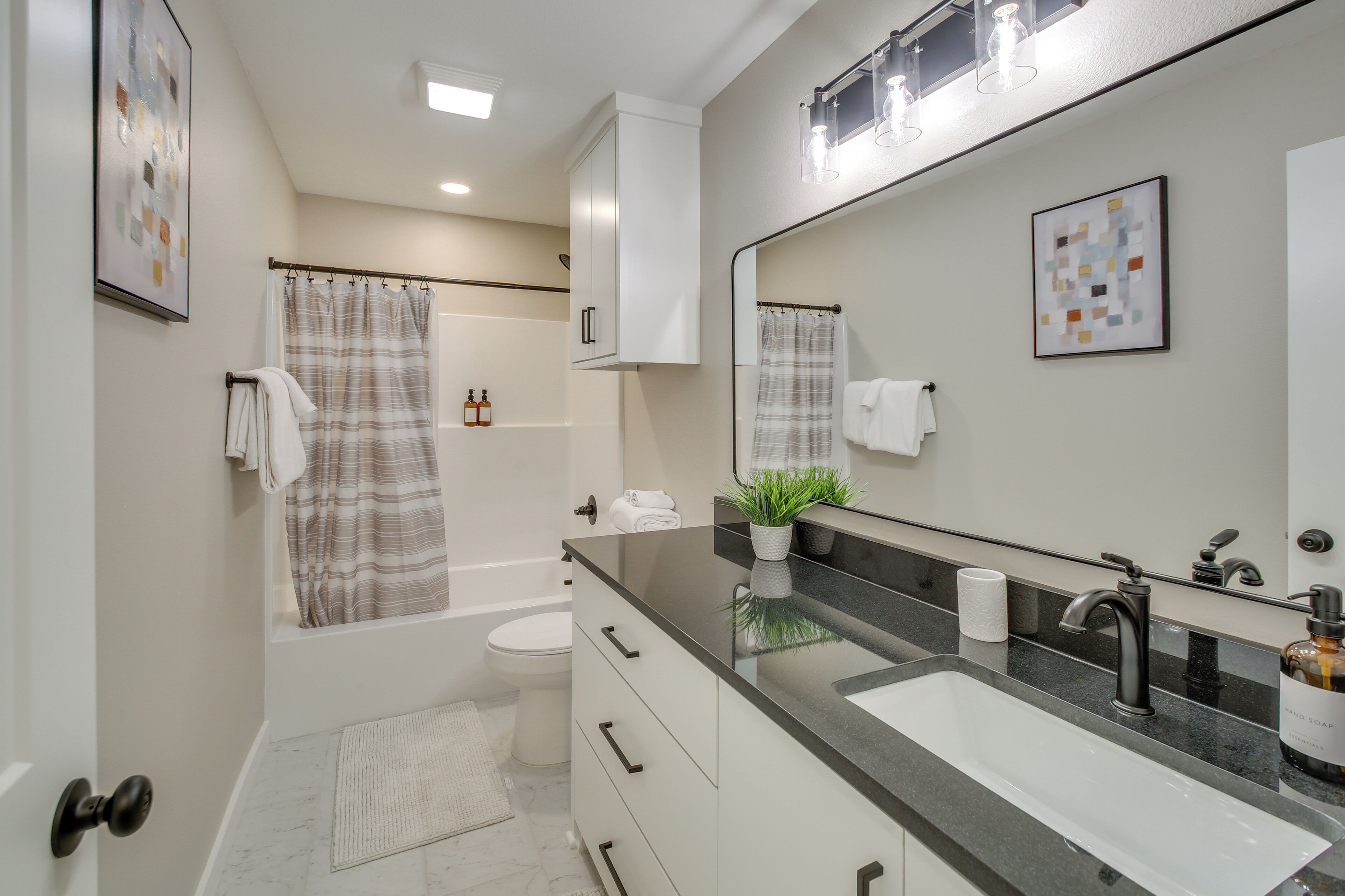 Une salle de bain moderne avec un grand miroir, un lavabo sur un plan de toilette noir, des toilettes et un espace douche.
