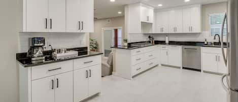 A modern kitchen with white cabinets, black countertops, and stainless steel appliances.