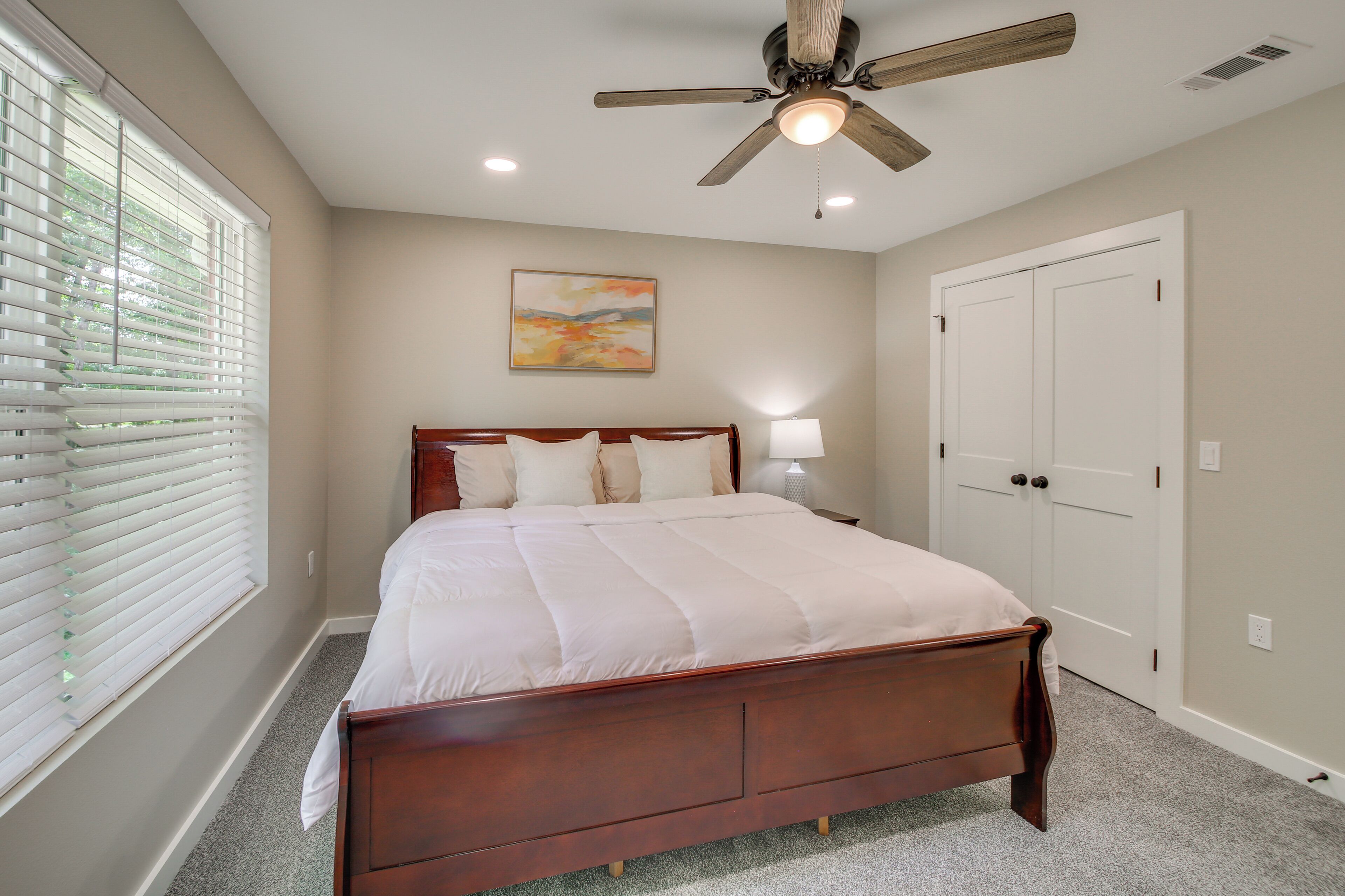 Une chambre à coucher avec un lit en bois, un ventilateur de plafond, une table de chevet avec une lampe et une porte.