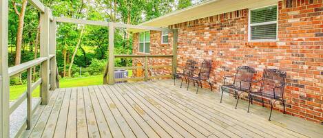 A wooden deck with metal chairs, a brick wall, and a view of trees.