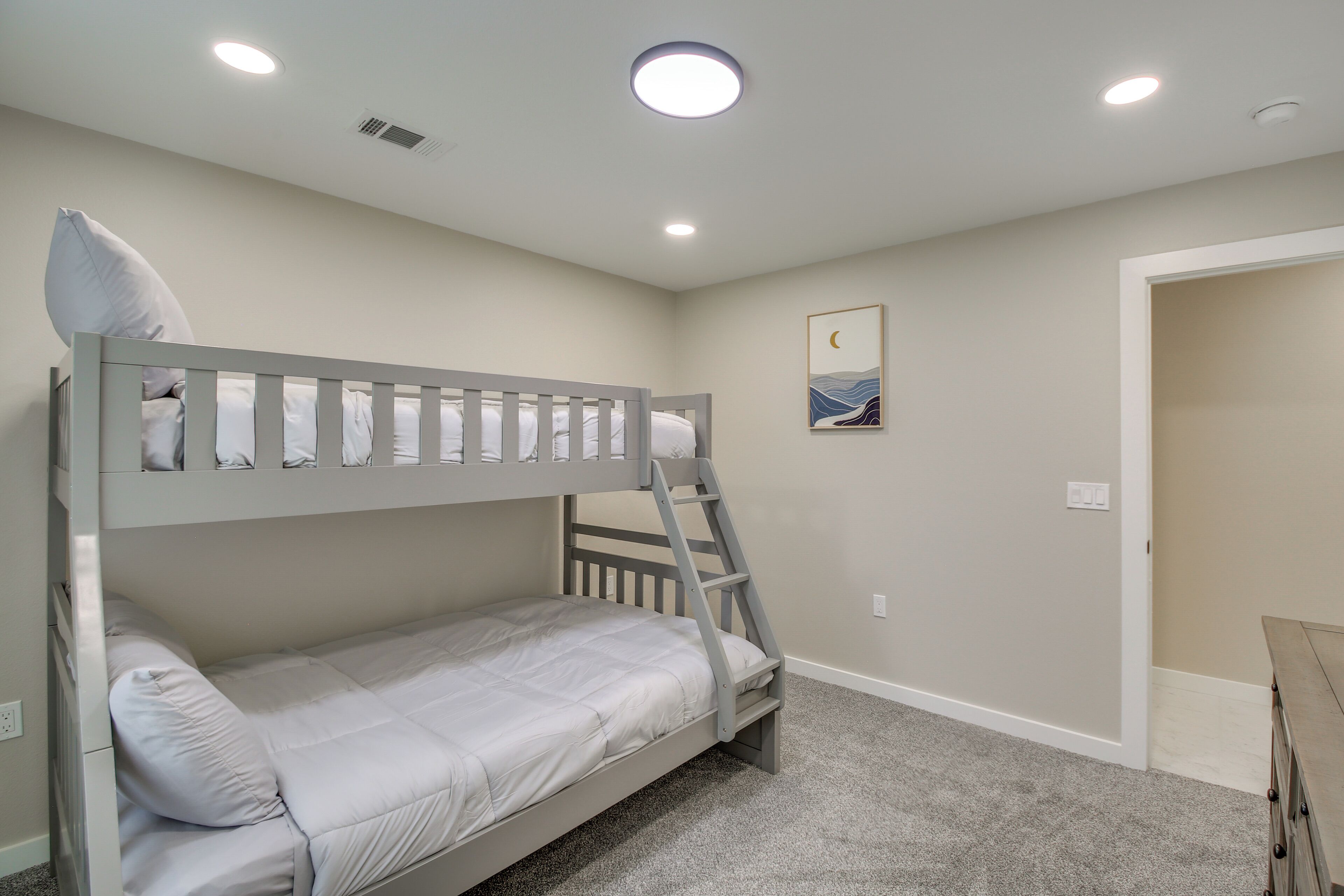A bunk bed with a ladder, a small painting on the wall, and a door to the right.