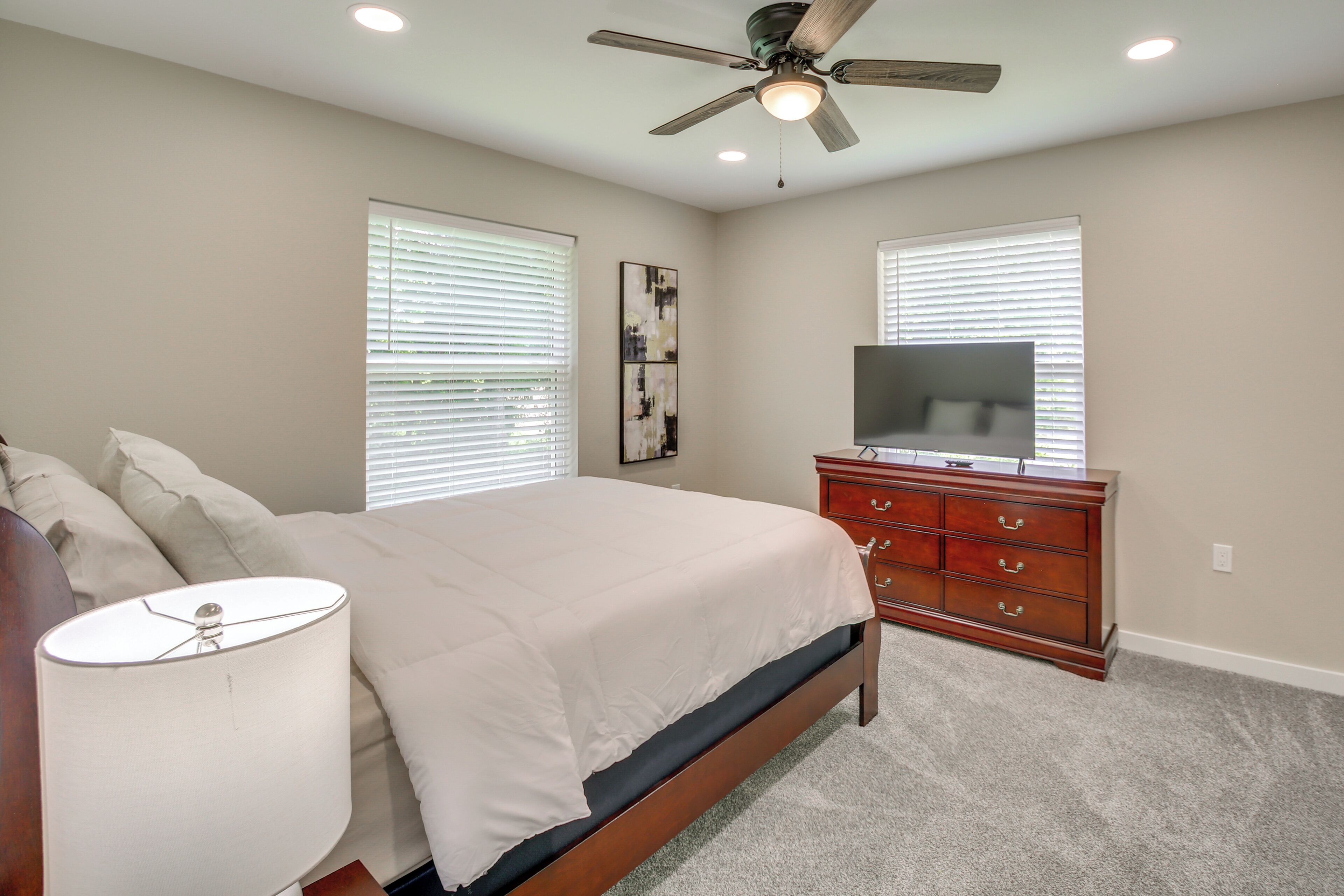 A bedroom with a bed, a dresser, a ceiling fan, and a TV.