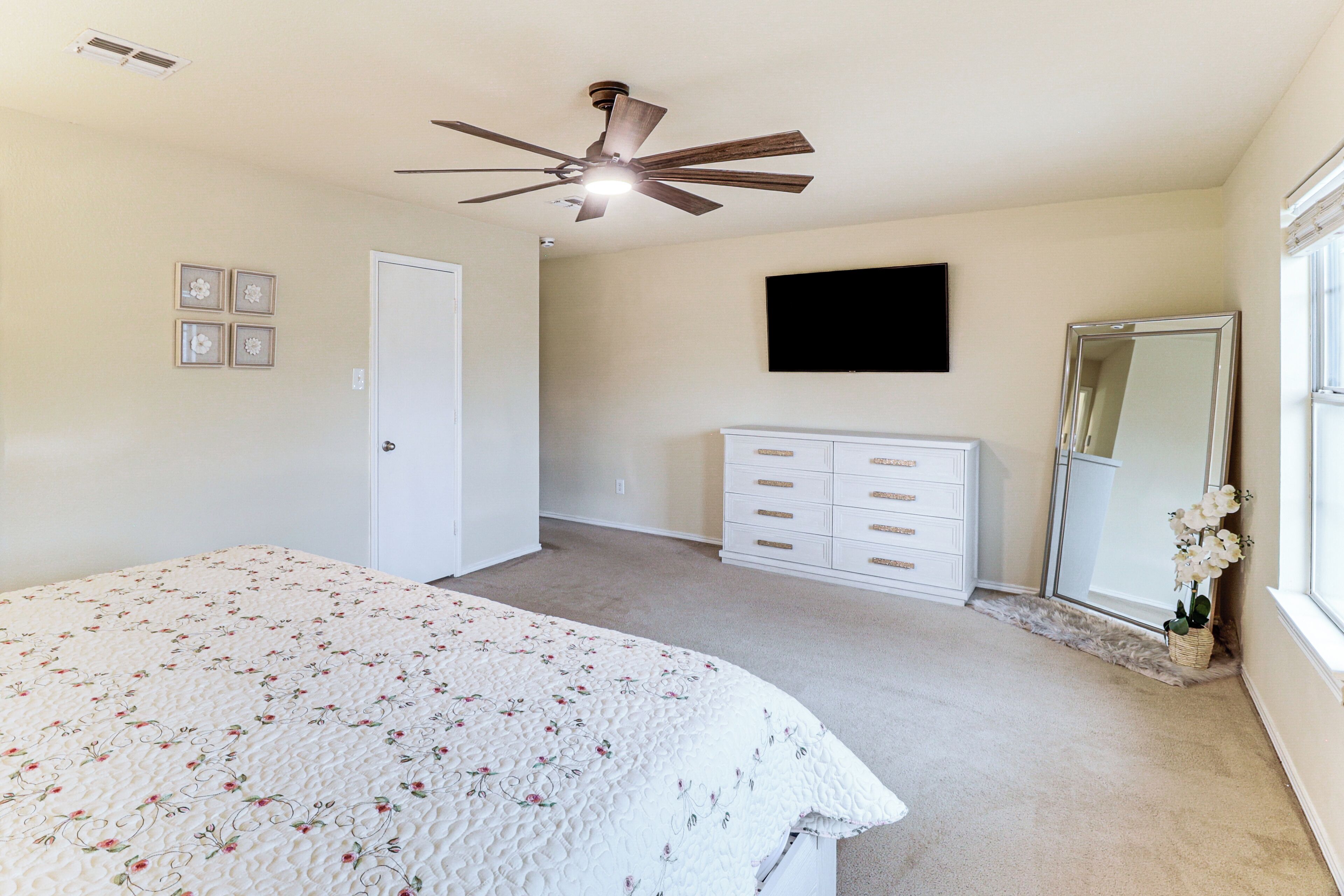 A bedroom with a bed, a ceiling fan, a dresser, a mirror, and a TV.