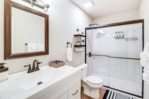 Une salle de bain avec un lavabo blanc, un miroir, des toilettes et une cabine de douche en verre.