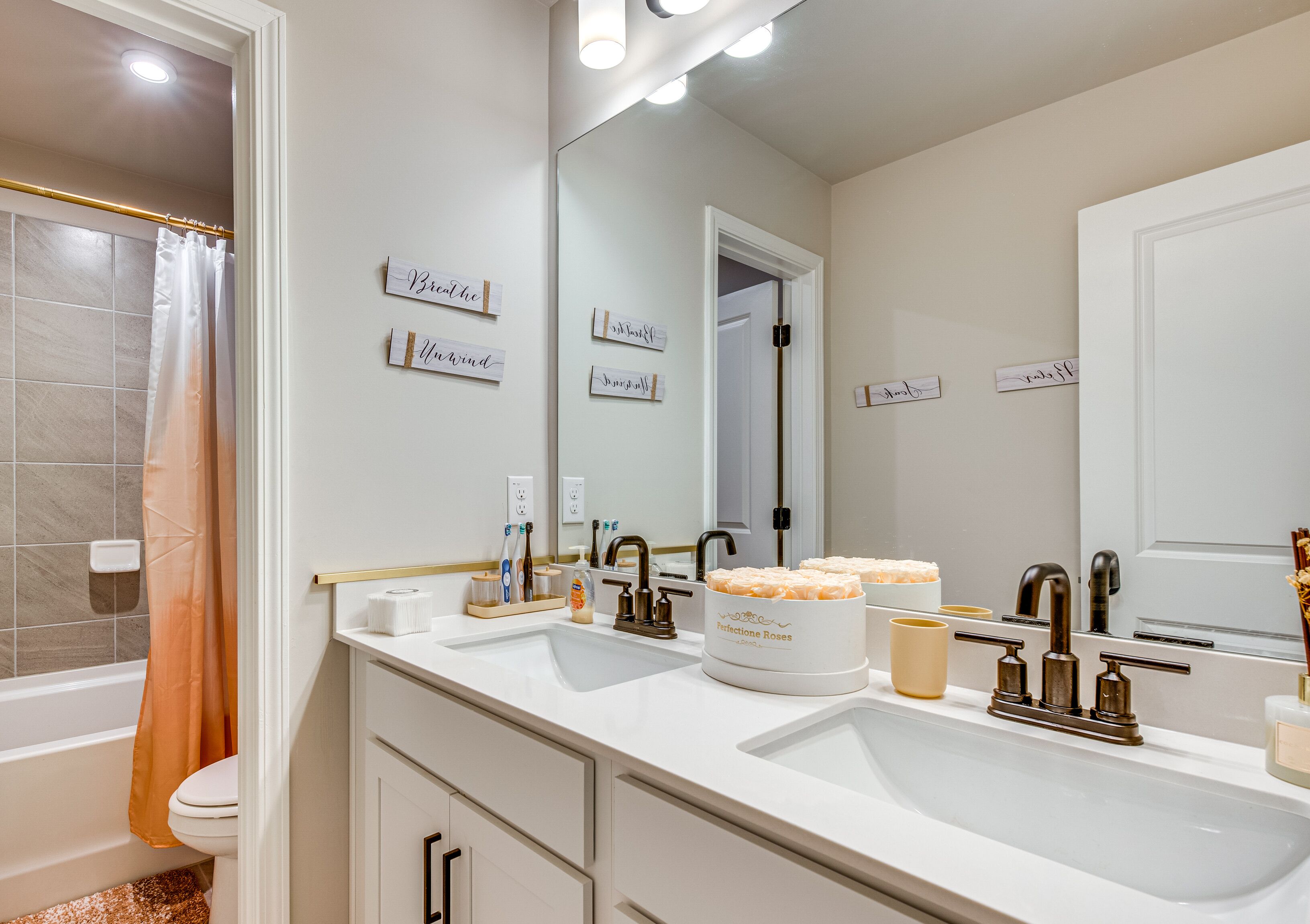 A modern bathroom with a bathtub, toilet, and sink. There are decorative signs on the wall and a large mirror above the sink.