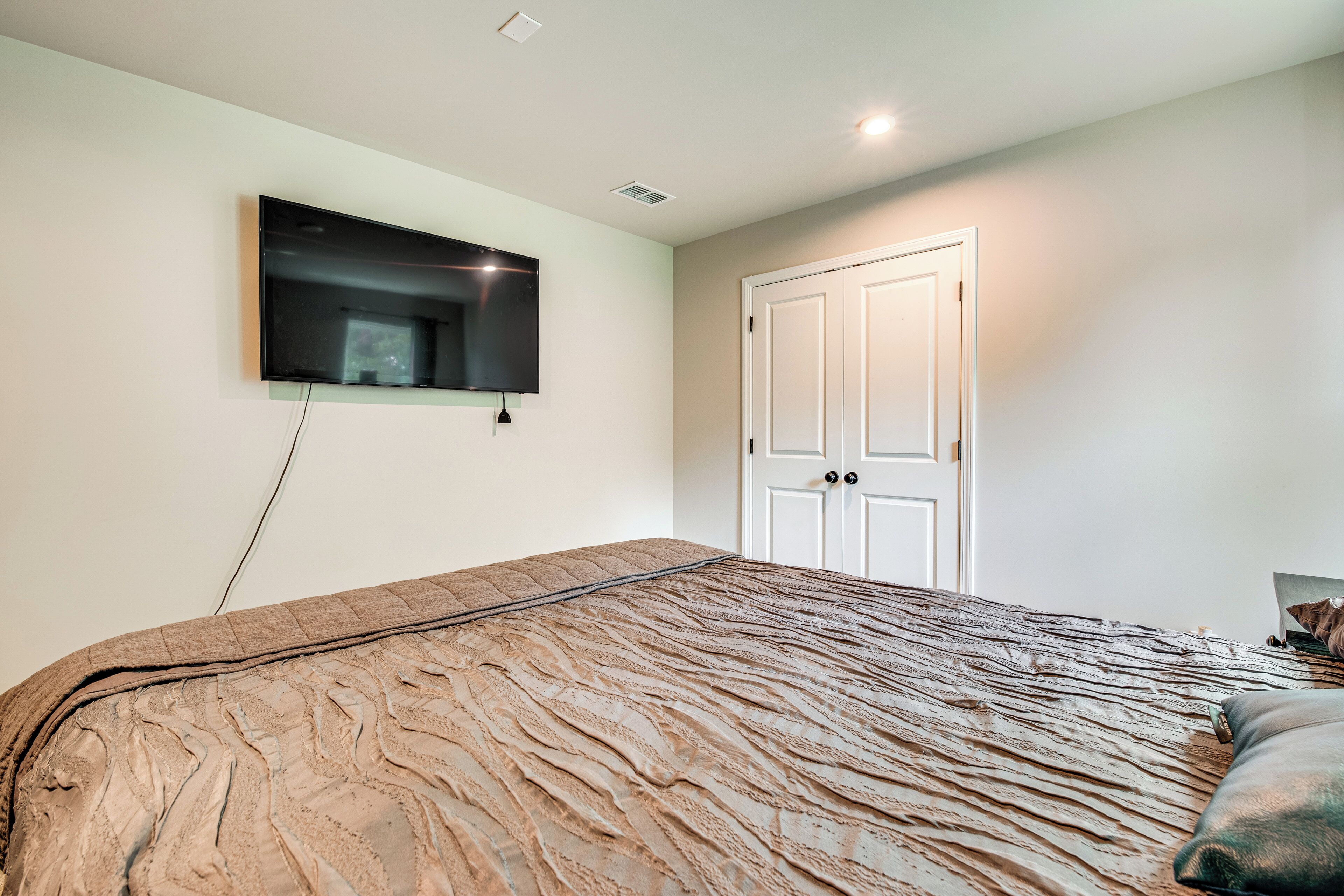 A bedroom with a bed, a mounted TV, a door, and a laptop on a table.