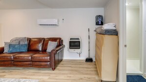 A living room with a brown leather sofa, an air conditioner, a standing heater, and a broom. - Walk to Norfork Lake: Guest House in Henderson (Henderson)