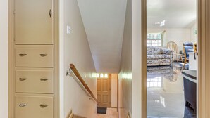 A hallway with a beige door, a staircase, and a view into a living room with patterned furniture and a black countertop. - 1 Mi to Dtwn Salem: Apt w/ Garage Access! (Salem)