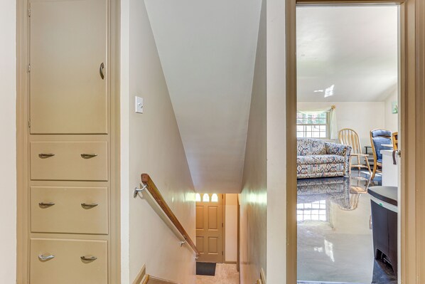 A hallway with a beige door, a staircase, and a view into a living room with patterned furniture and a black countertop. - 1 Mi to Dtwn Salem: Apt w/ Garage Access! (Salem)
