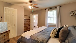 A bedroom with a bed, a ceiling fan, a window with curtains, a dresser, and a door. - 16 Mi to Dtwn Jackson: Quiet Southern Escape (Terry)
