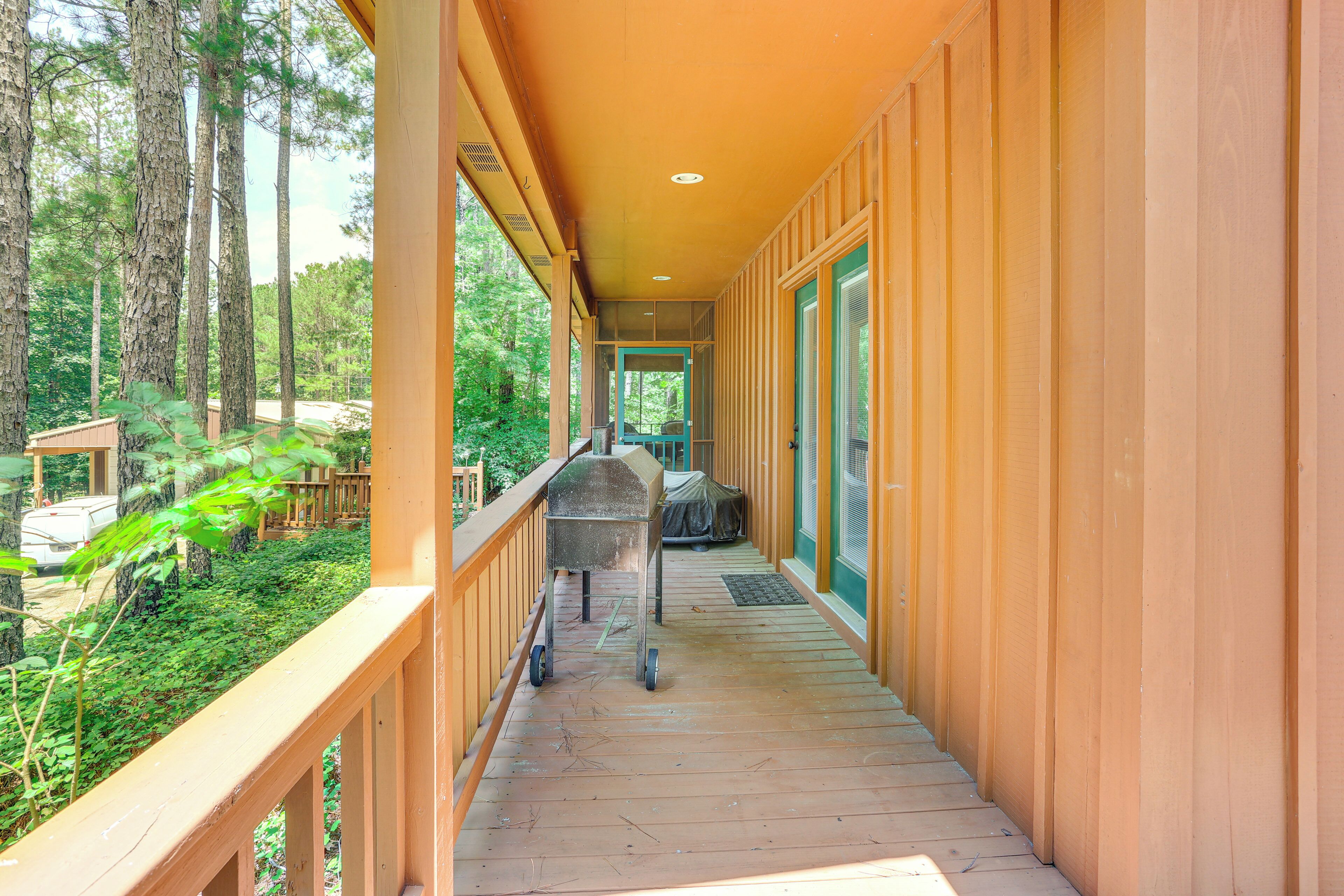 A covered wooden deck with a barbecue grill, surrounded by trees.