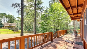 A wooden deck with a railing, overlooking a forested area with a cabin in the background. - Pickwick Lake Cabin w/ Private Marina Access (Iuka)