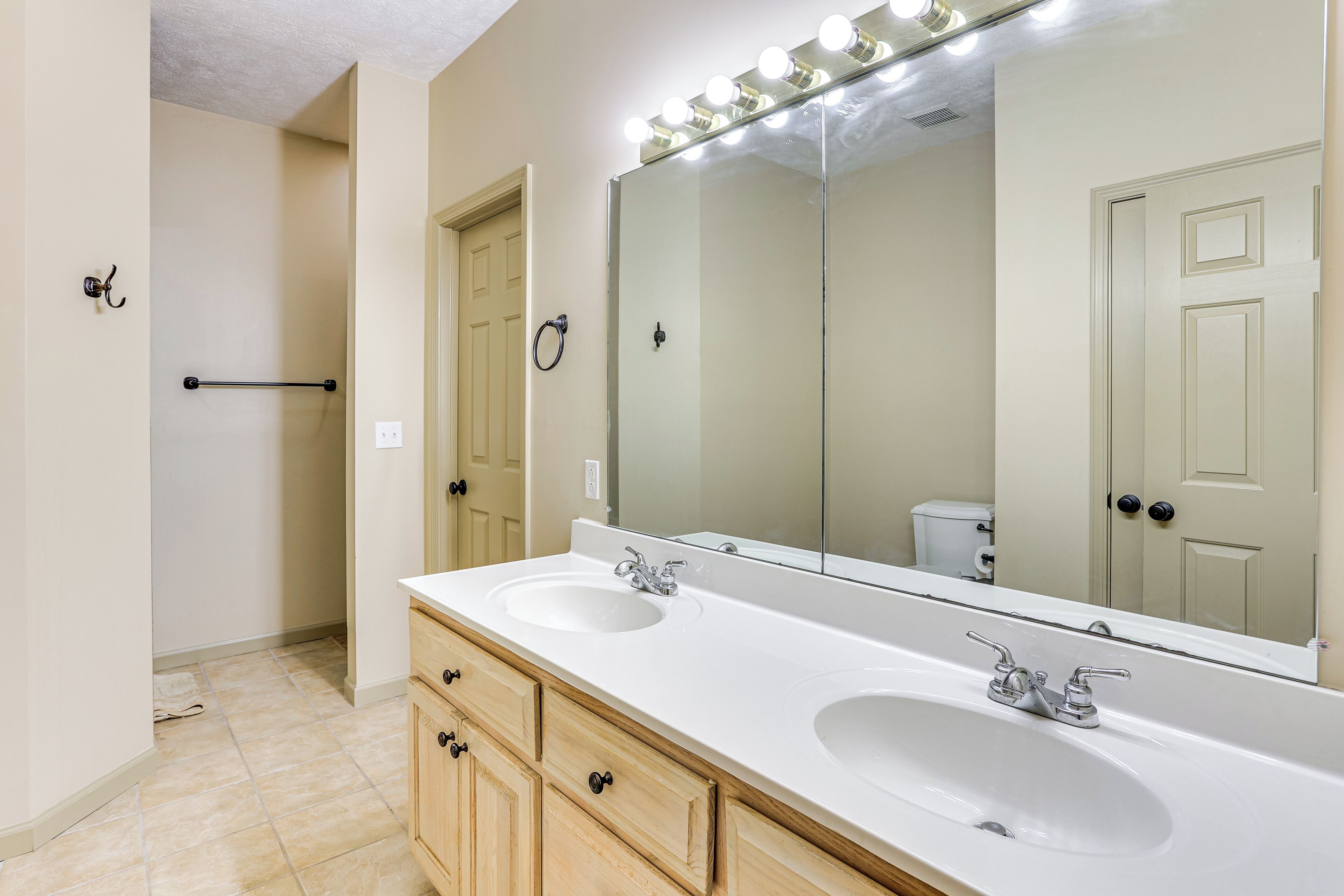 Un baño con lavamanos doble, un espejo grande con luces y un perchero para toallas.