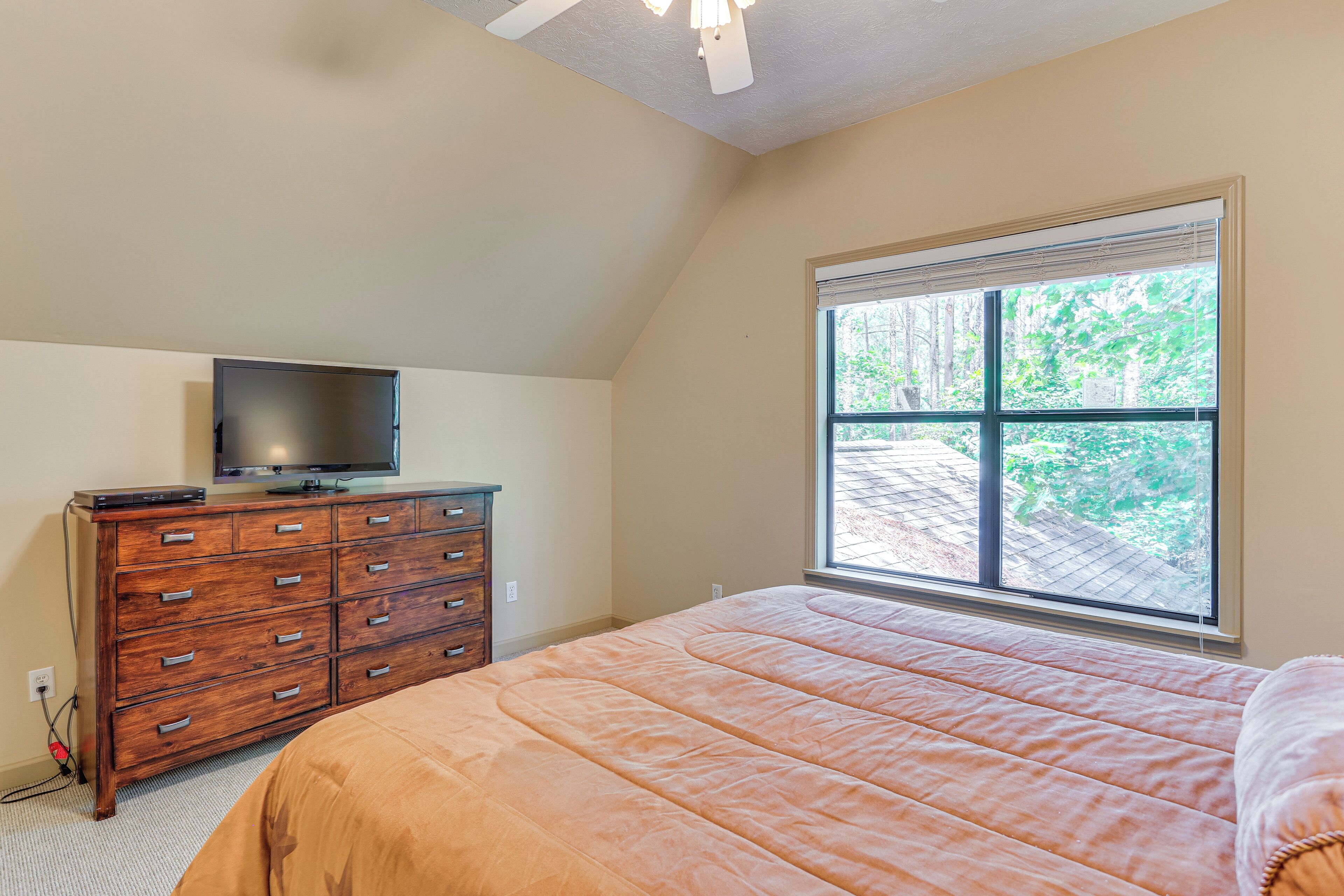 Un dormitorio con una ventana grande, una cama, un aparador y un televisor.