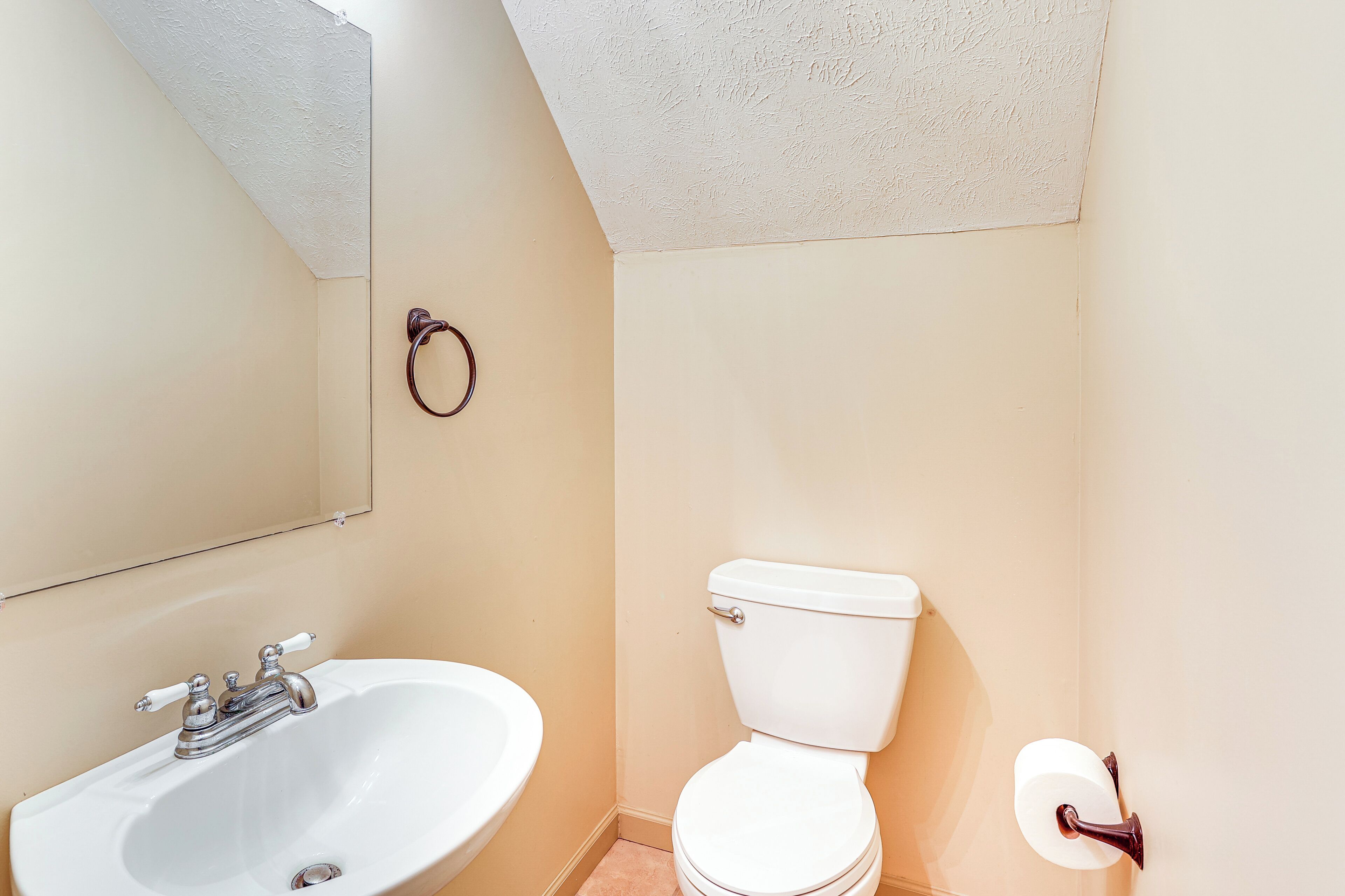 A bathroom with a white sink, toilet, and a towel ring on the wall.