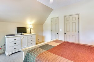 Un dormitorio con cama, cómoda, televisor y dos puertas.
