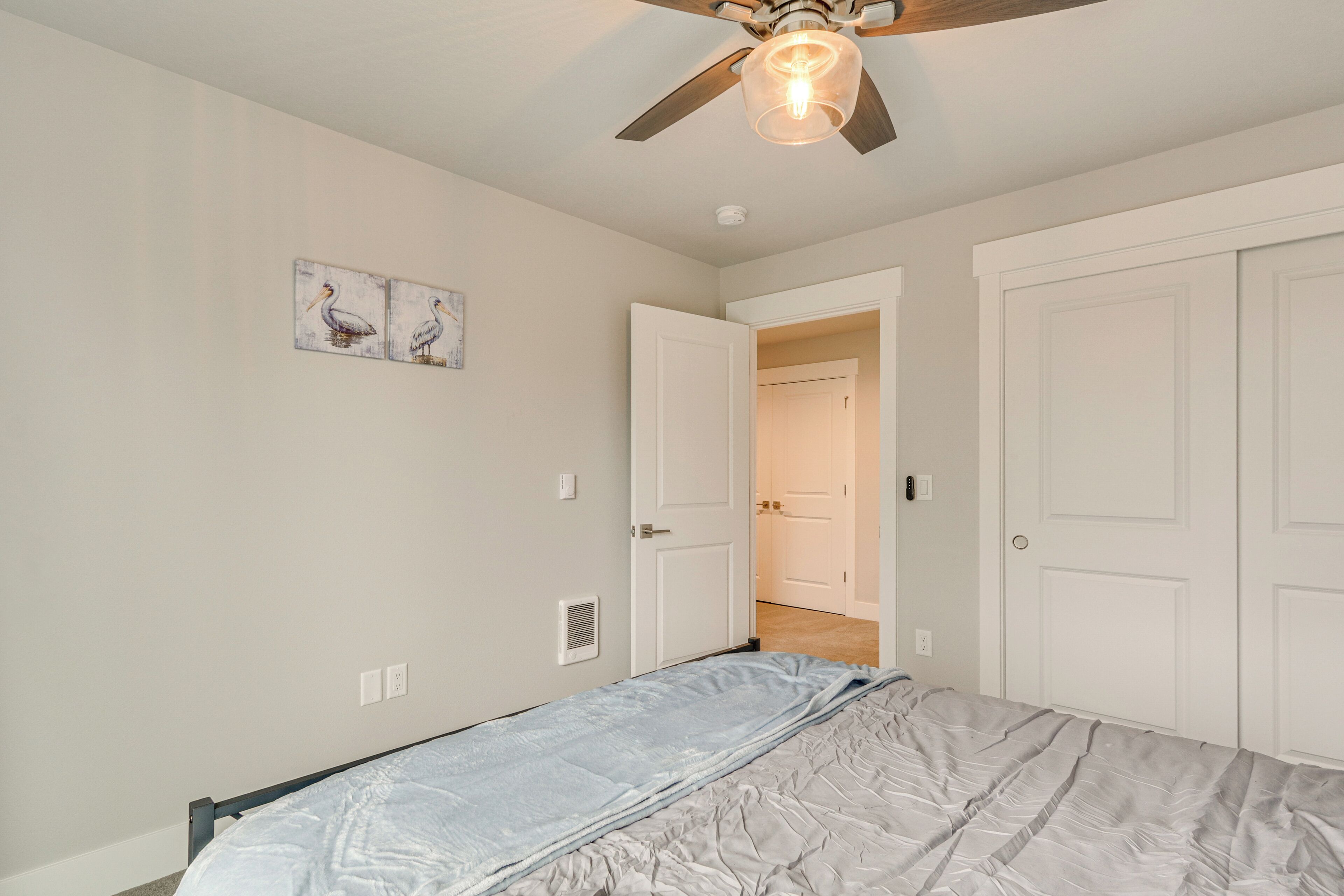 A bedroom with a bed, a ceiling fan, white doors, and a hallway leading to another room.