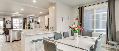 A modern kitchen with white cabinetry, a central island, and a dining area with a white table and grey chairs.