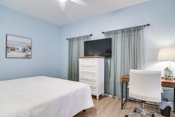 Une chambre à coucher comprenant un lit, une commode, un bureau avec une chaise, une lampe et un tableau accroché au mur.